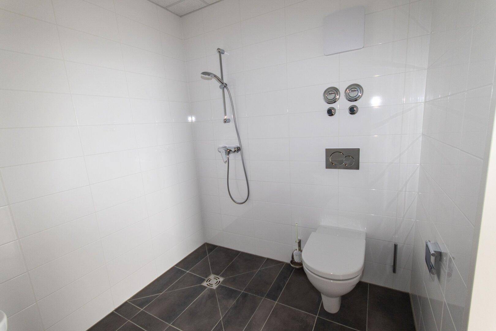 Modernes Badezimmer mit Dusche und wandhängendem WC, komplett gefliest in Weiß und Grau.