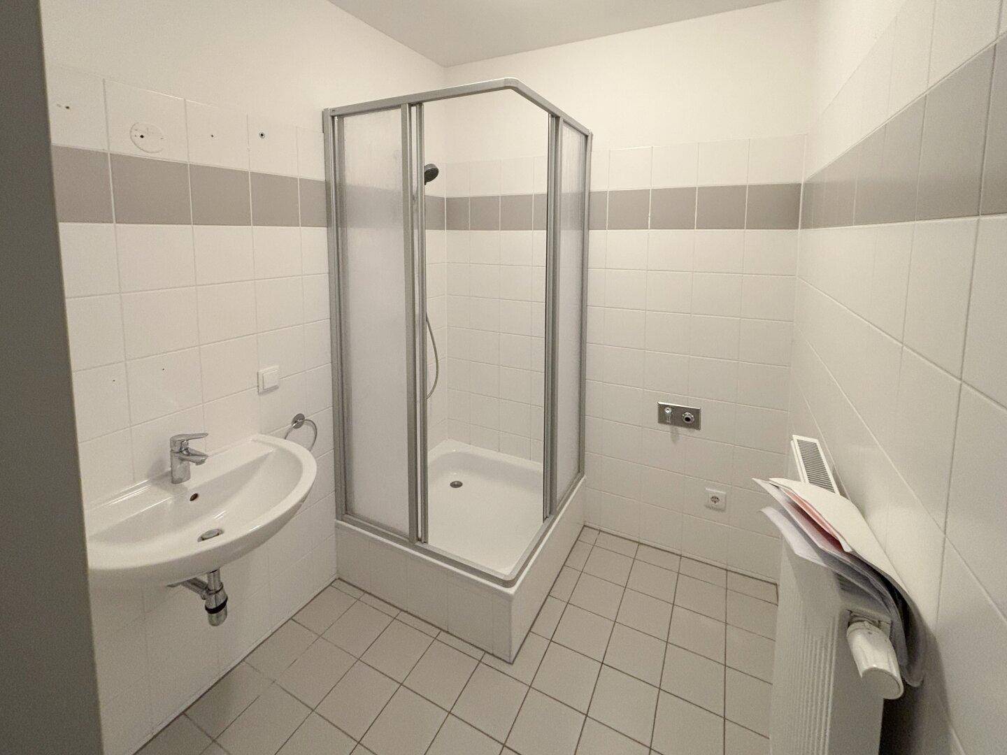 Funktionales Badezimmer mit Duschkabine, Waschbecken und weißen Fliesen mit grauen Akzenten.