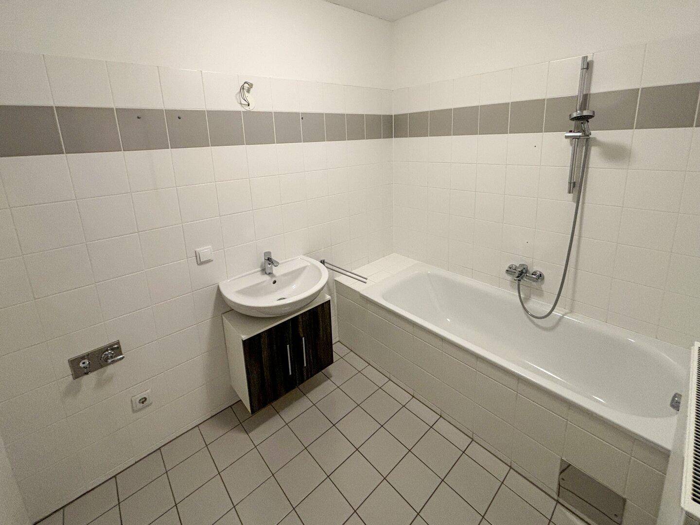 Funktionales Badezimmer mit Badewanne, Duschvorrichtung und Waschbeckenunterschrank.