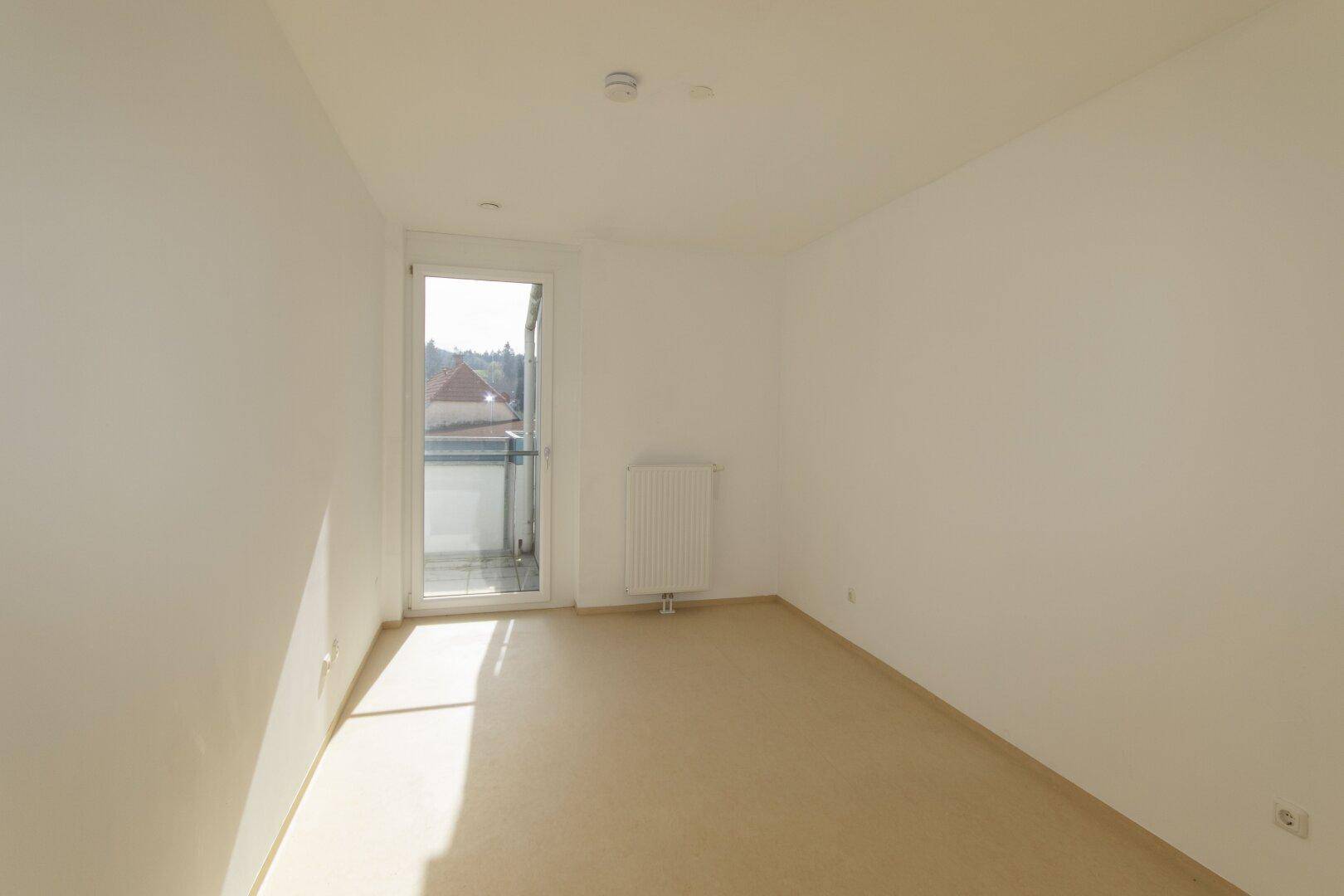 Helles Zimmer mit Zugang zu einem kleinen Balkon und Heizkörper.
