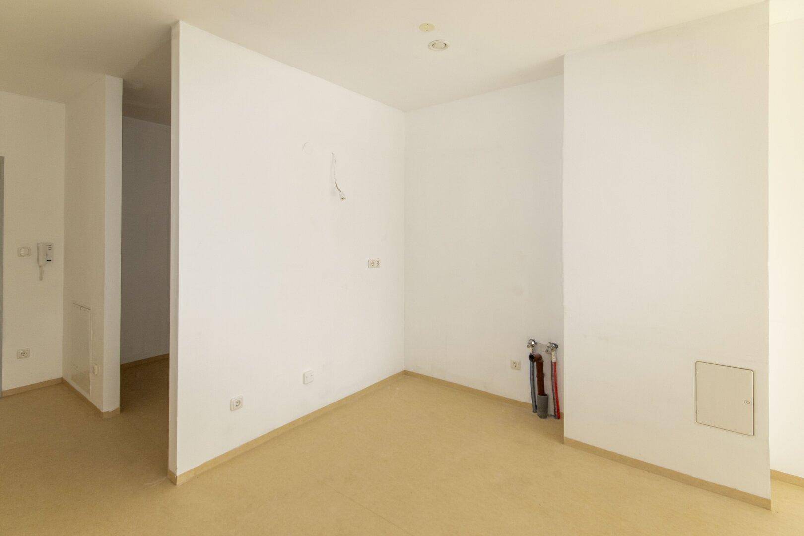 Leerer Küchenbereich mit Anschlüssen für Spüle und Geräte.