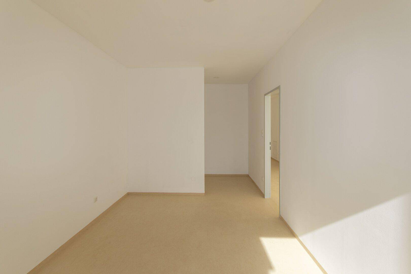 Heller, leerer Raum mit Durchgang zu einem weiteren Zimmer.