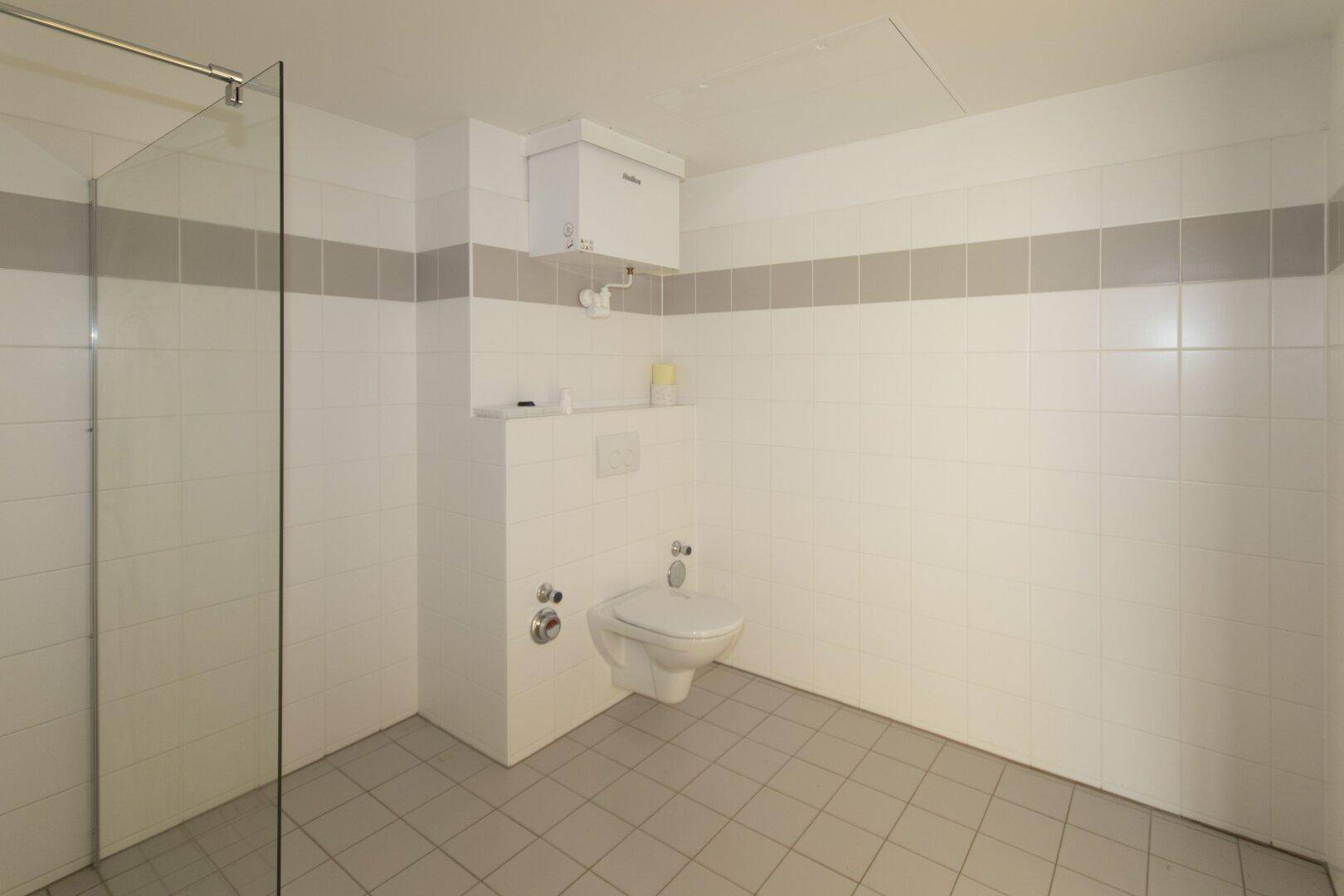 Geräumiges Badezimmer mit gefliesten Wänden, Dusche und wandhängendem WC.