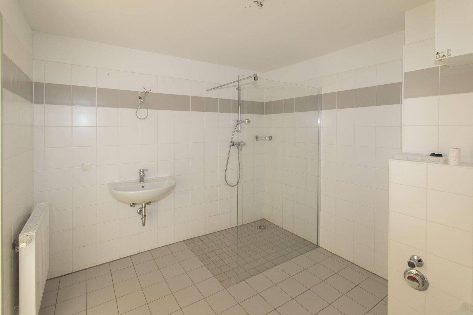 Helles Badezimmer mit Duschbereich, Waschbecken und Heizkörper.