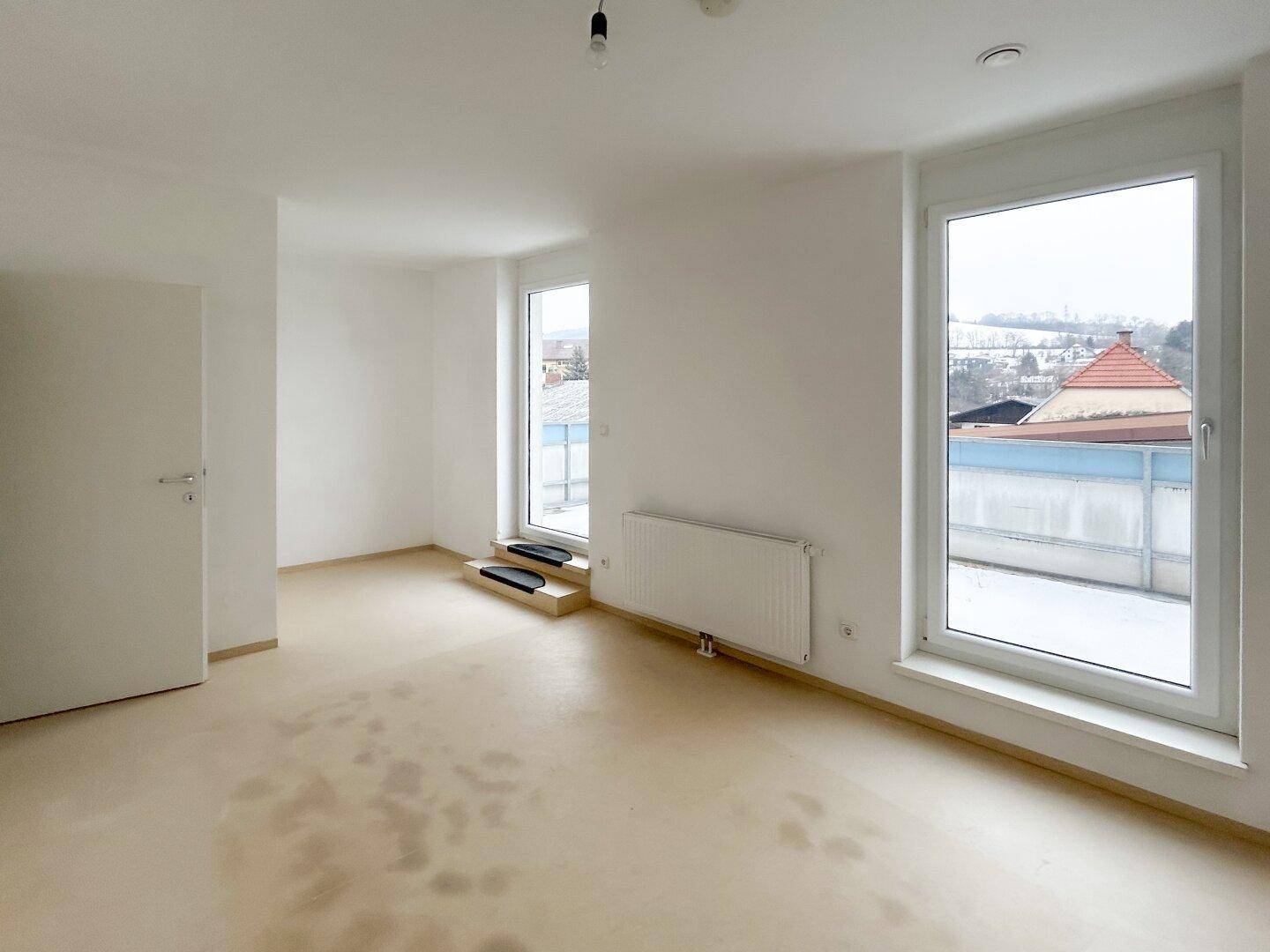 Lichtdurchfluteter Wohnraum mit großen Fenstern und Blick auf die Umgebung, ideal für helle Einrichtung.