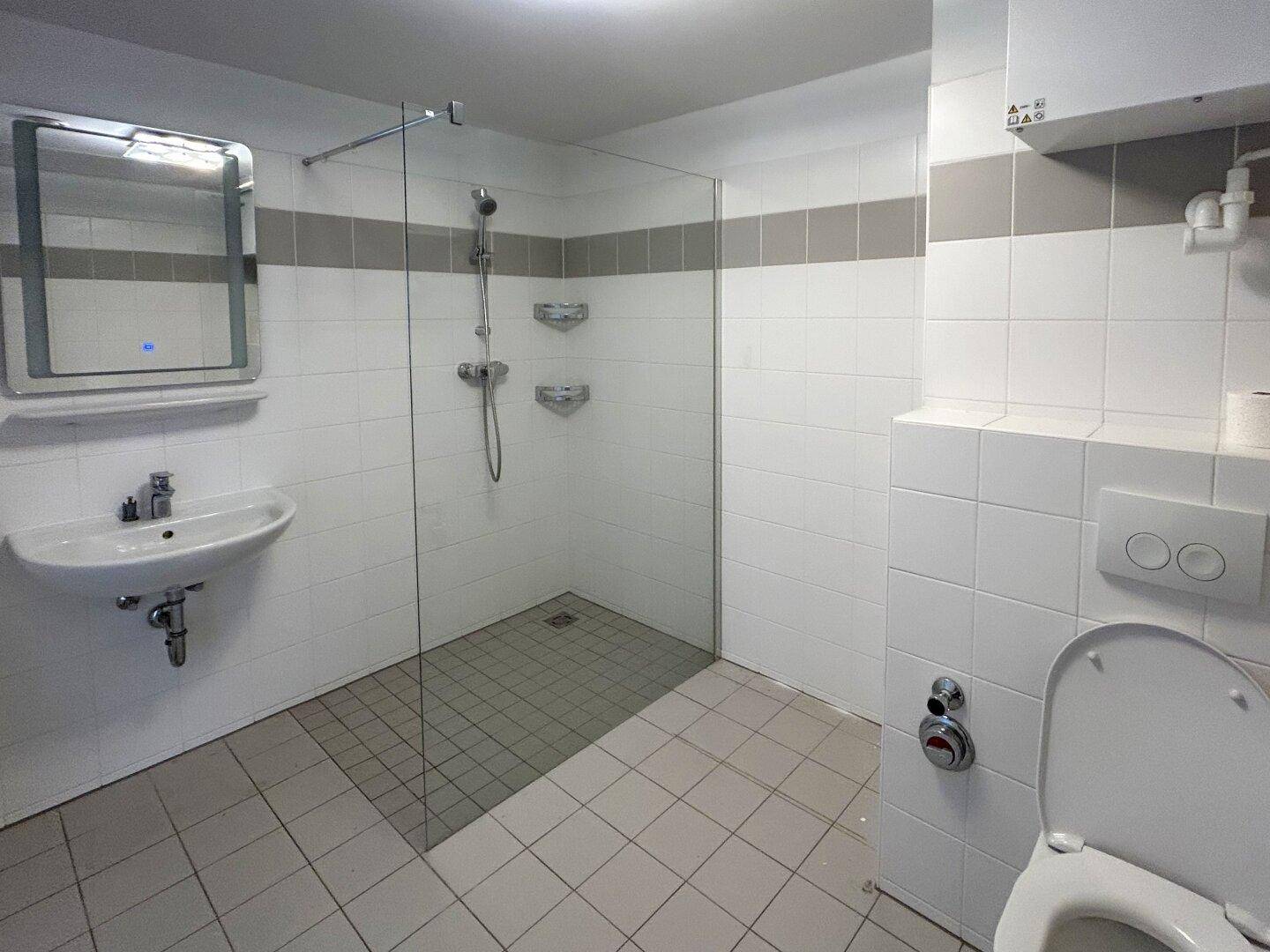 Modernes Badezimmer mit begehbarer Dusche, WC und Waschbecken, in hellen Fliesen gehalten.