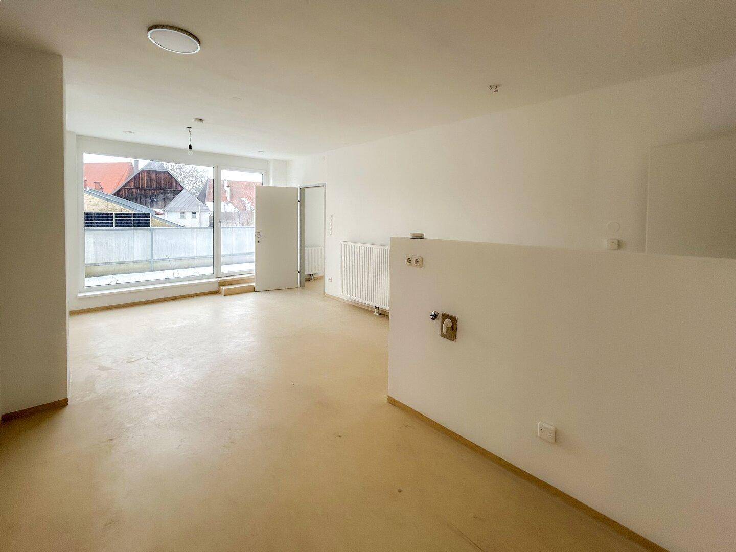 Heller, leerer Wohnbereich mit großen Fenstern und Zugang zur Terrasse, bereit zur individuellen Gestaltung.