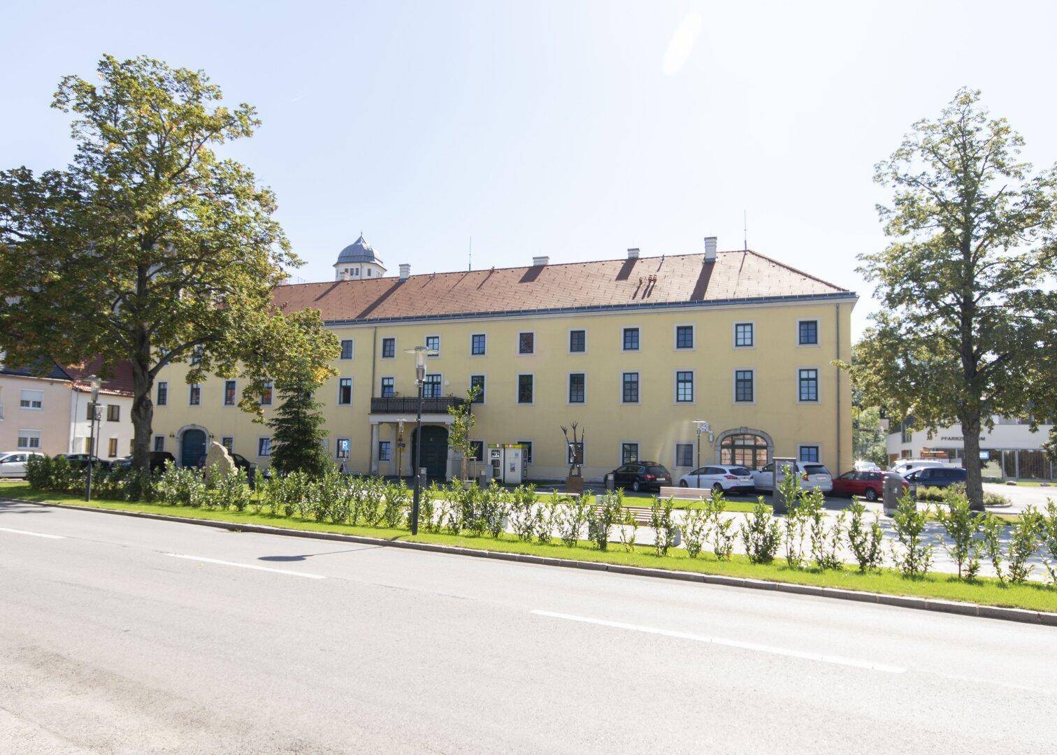 Historisches Gebäude mit gelber Fassade und vielen Fenstern, umgeben von Bäumen.