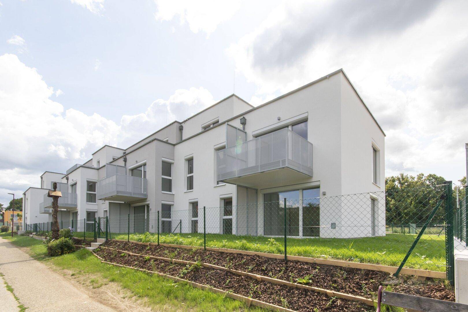 Reihenhausanlage mit moderner Architektur, Balkonen und einem grünen Gartenbereich im Vordergrund.