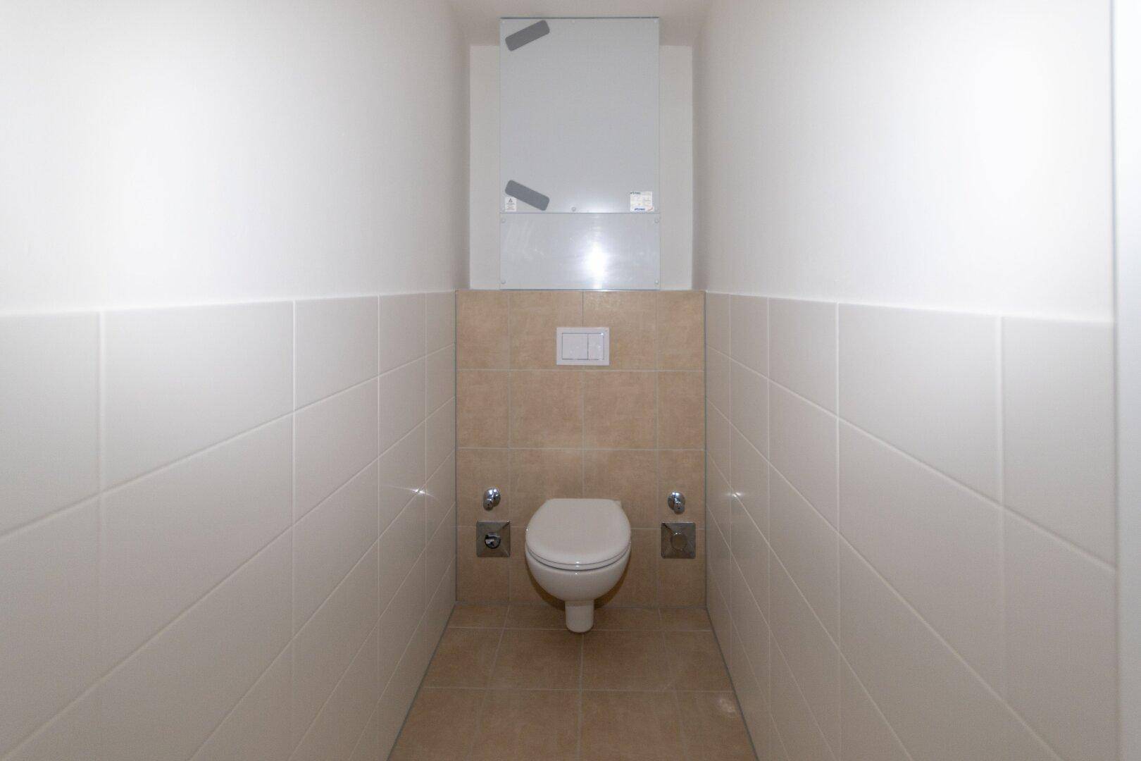 Separates WC mit wandhängender Toilette und modernen Fliesen in Weiß und Beige.