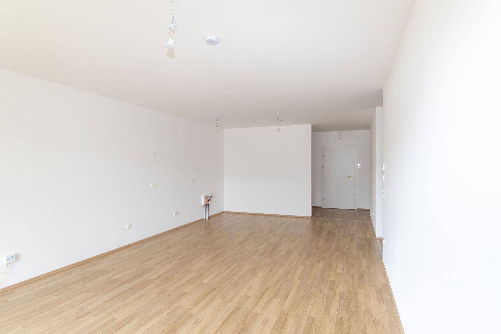 Heller, leerer Raum mit neuem Laminatboden und weißen Wänden, bereit zur individuellen Gestaltung.