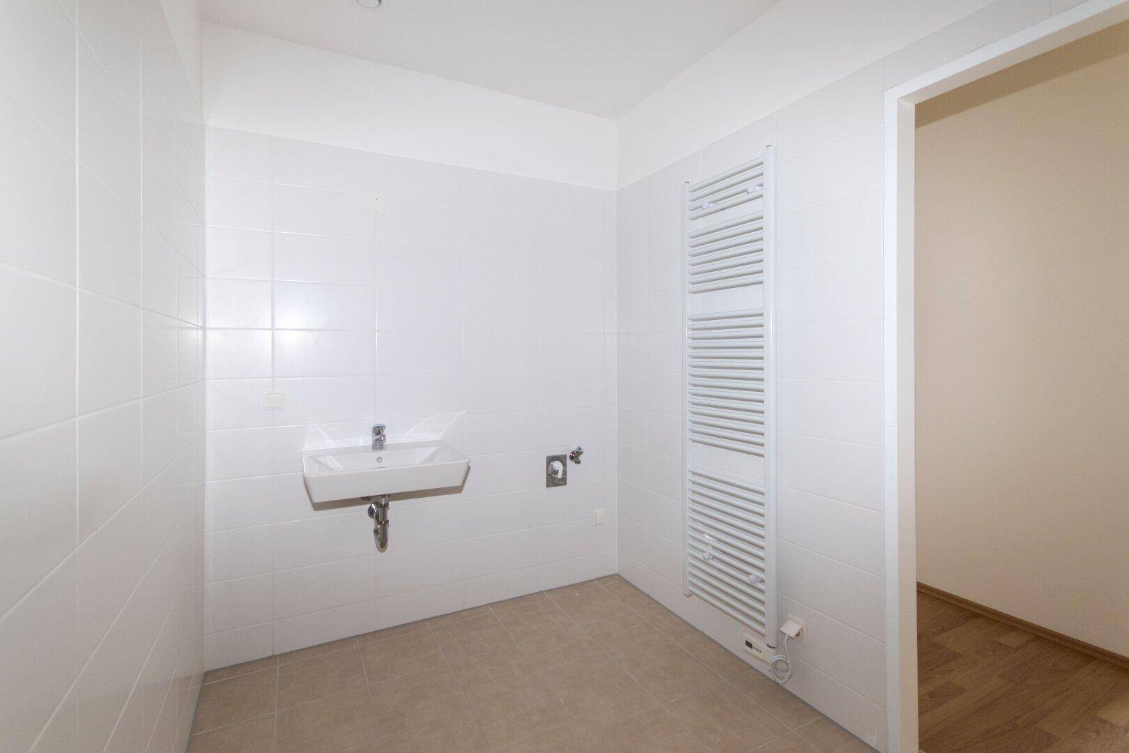 Modernes Badezimmer mit weißen Fliesen, Einzelwaschbecken und beheiztem Handtuchhalter.