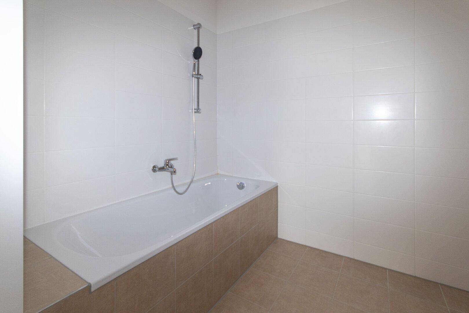 Badezimmer mit eingebauter Badewanne und weißen Wandfliesen, bereit zur Nutzung.