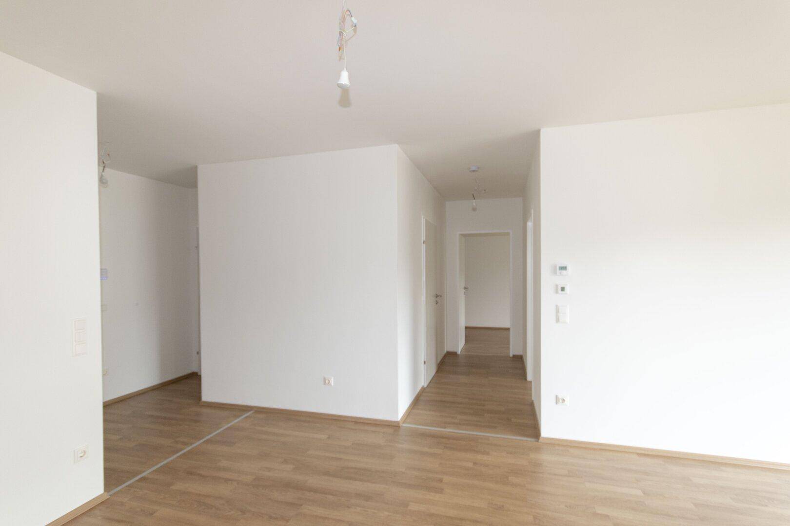 Heller Flur mit Laminatboden und weißen Wänden, der zu weiteren Räumen führt.