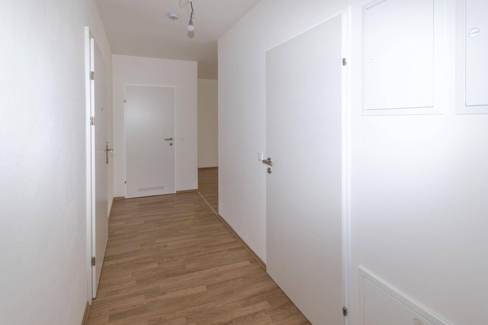 Langer, heller Flur mit mehreren weißen Türen und durchgehendem Laminatboden in einem modernen Gebäude.