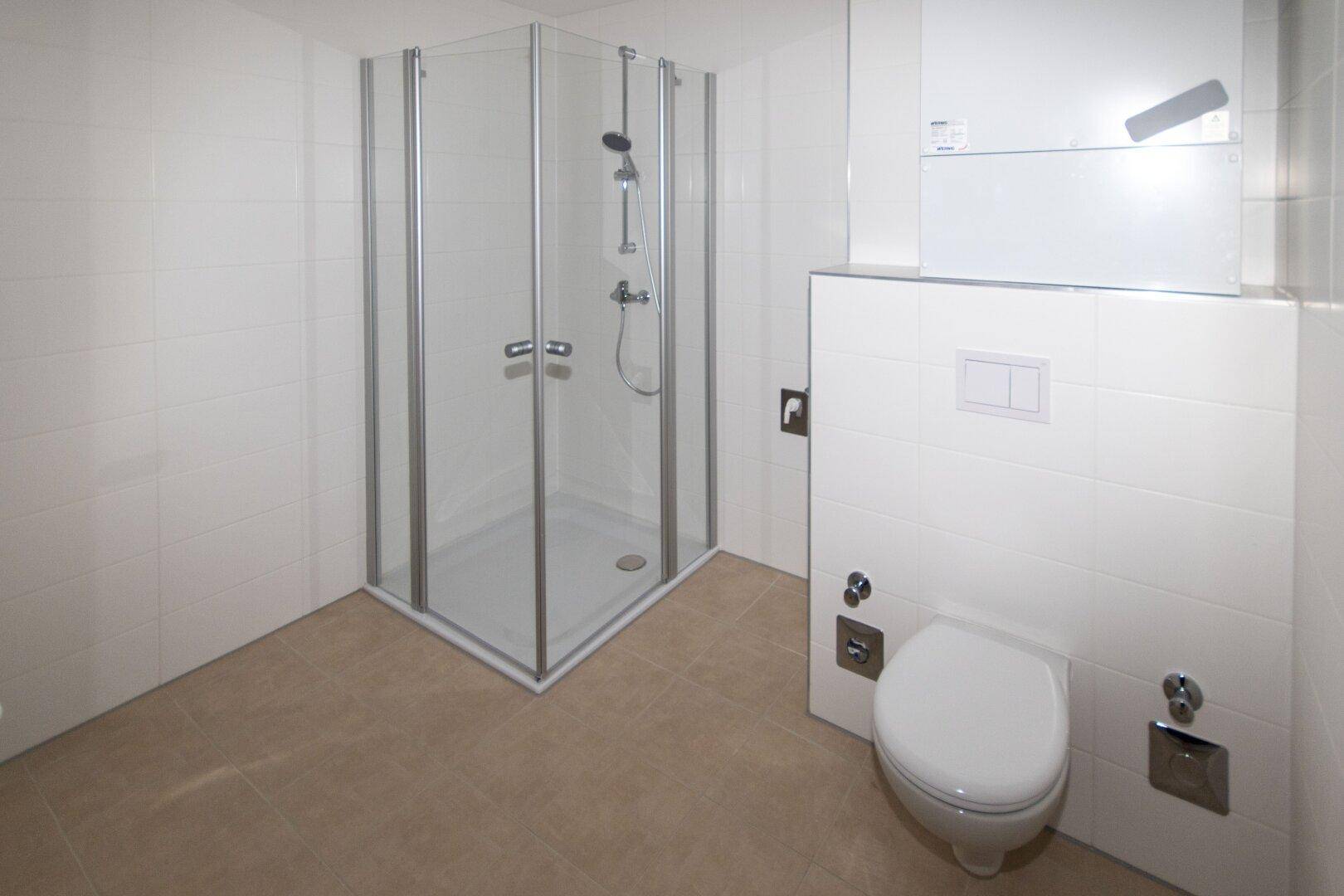 Modernes Badezimmer mit Eckdusche und wandhängendem WC, komplett gefliest in hellen Farbtönen.