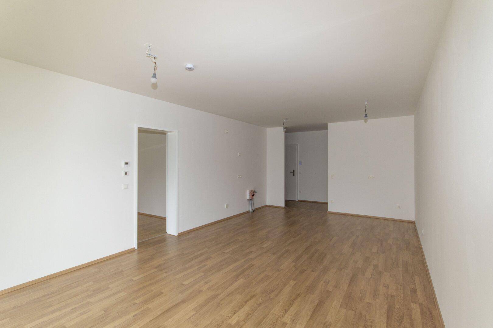 Heller, leerer Raum mit modernem Laminatboden und weißen Wänden, bereit für die individuelle Gestaltung.