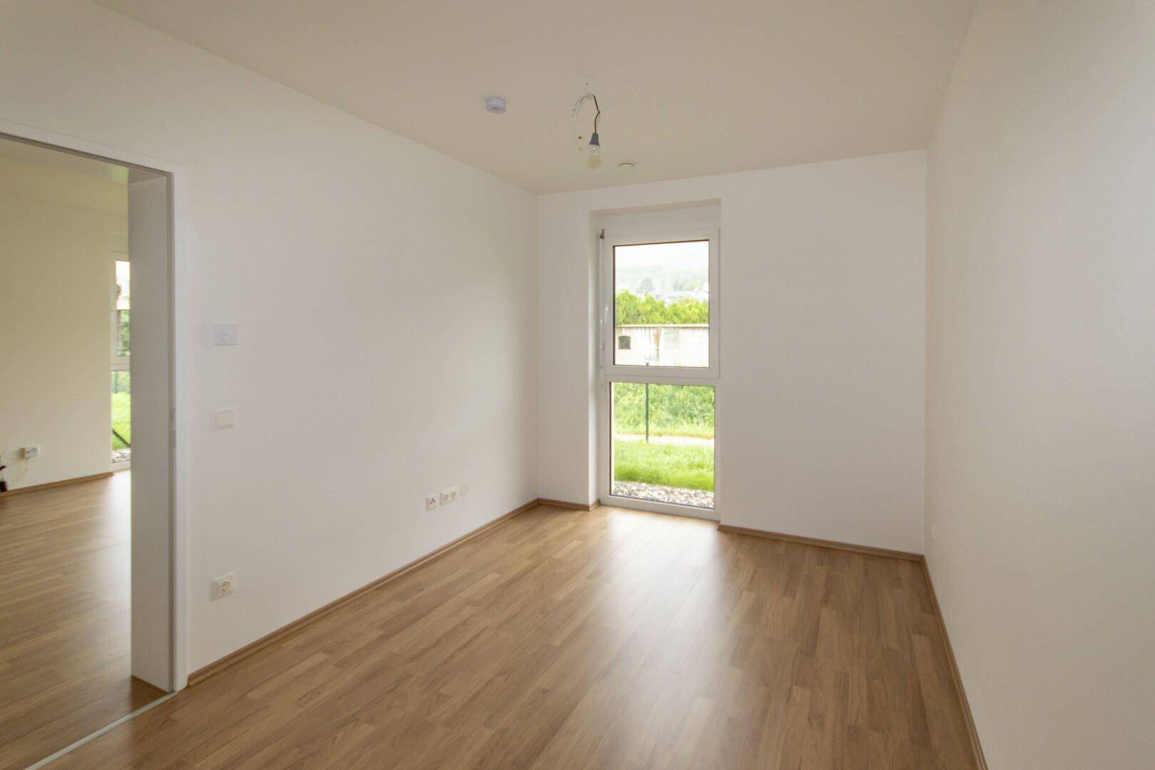 Helles Zimmer mit großem Fenster und Blick ins Grüne, ausgestattet mit modernem Laminatboden.