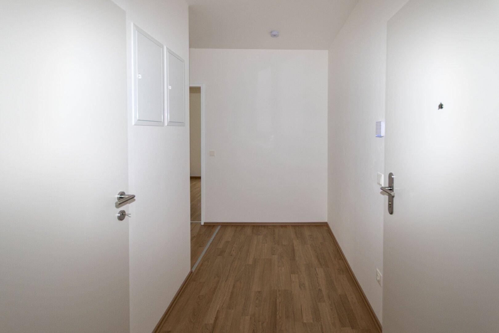 Heller Flur mit Laminatboden und weißen Türen, der zu weiteren Räumen führt.