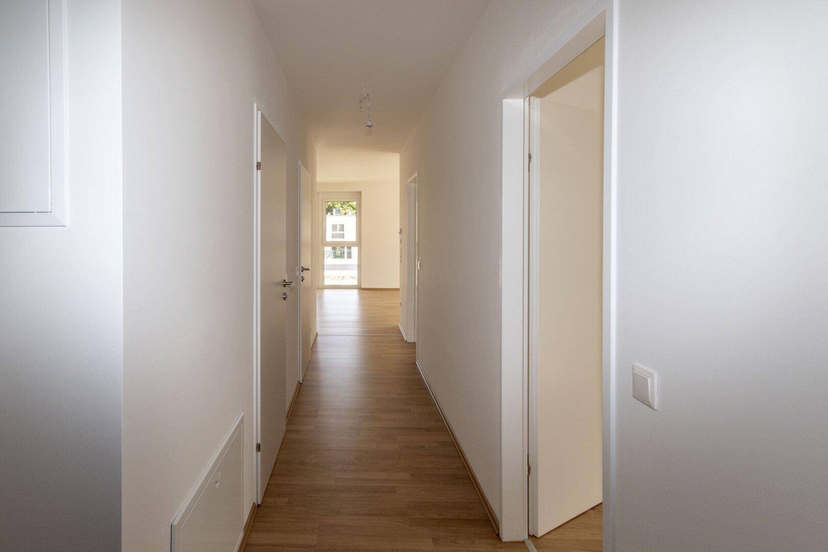 Langer, heller Flur mit Laminatboden und weißen Wänden, der die verschiedenen Wohnbereiche verbindet.
