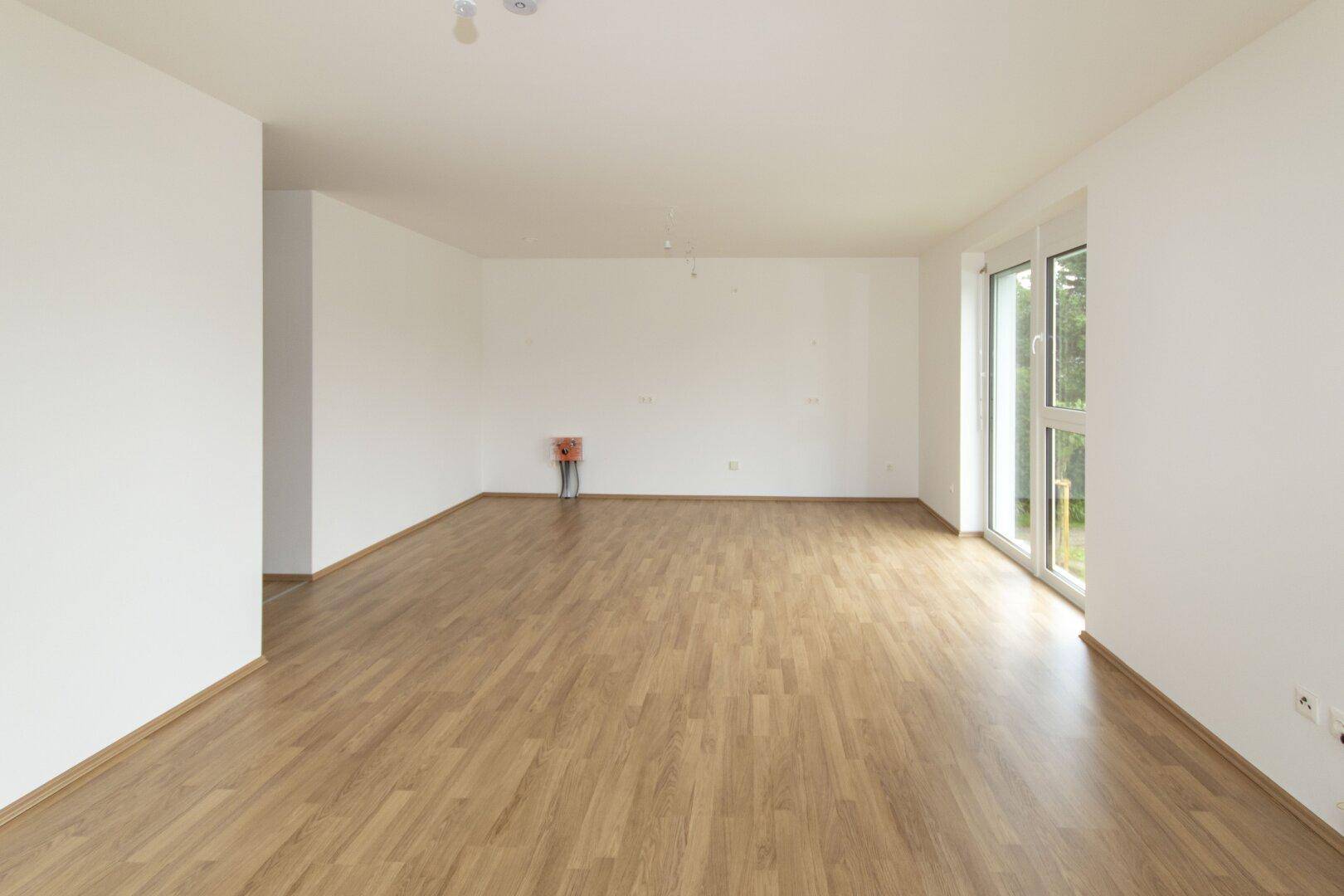 Lichtdurchfluteter Raum mit hellem Laminatboden und großen Fenstern, bereit zur Einrichtung.