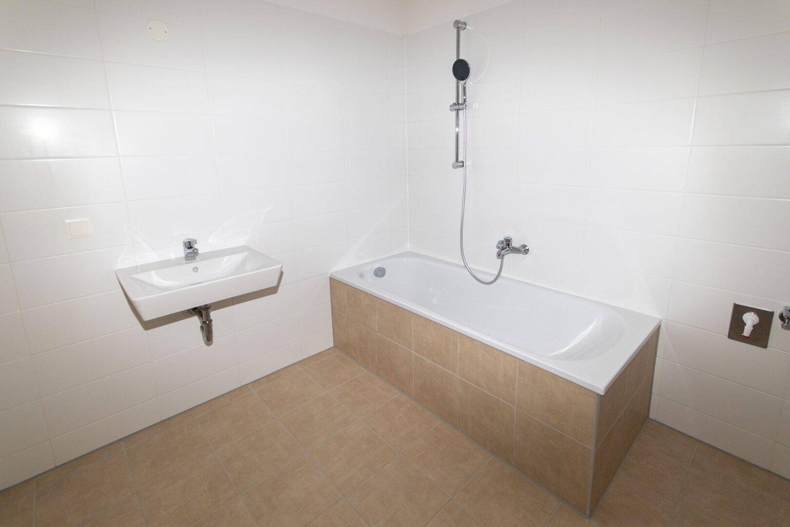 Modernes Badezimmer mit Badewanne, Waschbecken und hellen Fliesen an Wänden und Boden.
