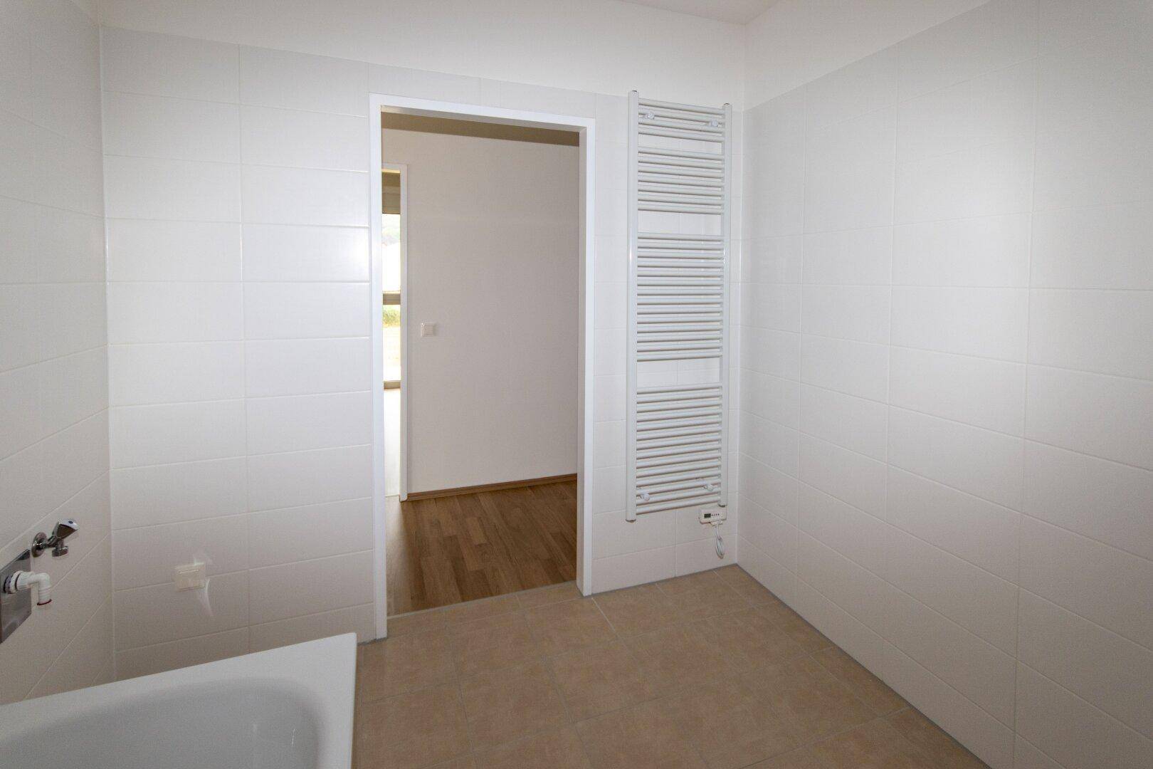 Badezimmer mit weißem Handtuchheizkörper und Zugang zu einem weiteren Raum.