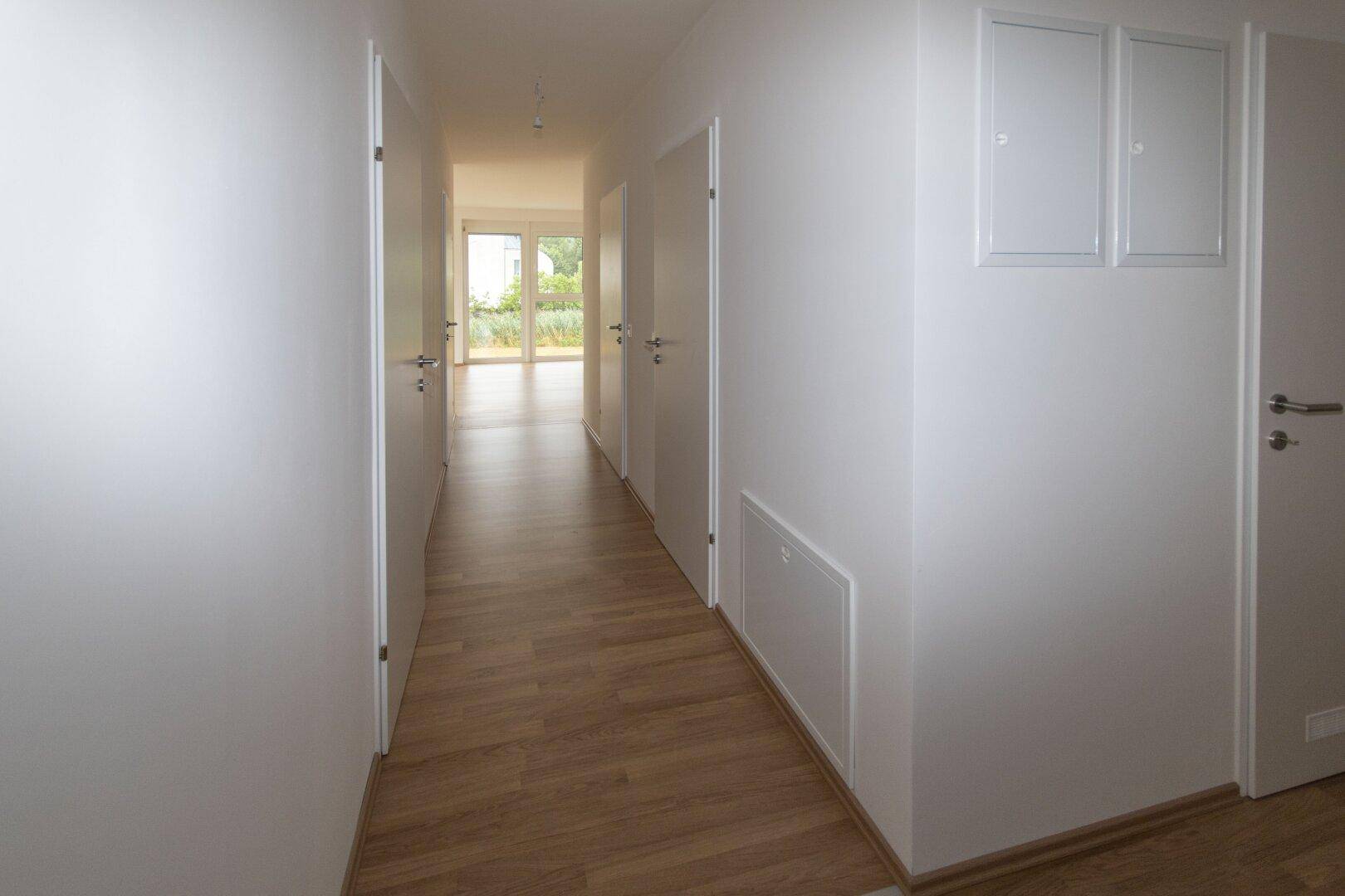 Langer, heller Flur mit Laminatboden und mehreren Türen, der die verschiedenen Wohnbereiche verbindet.