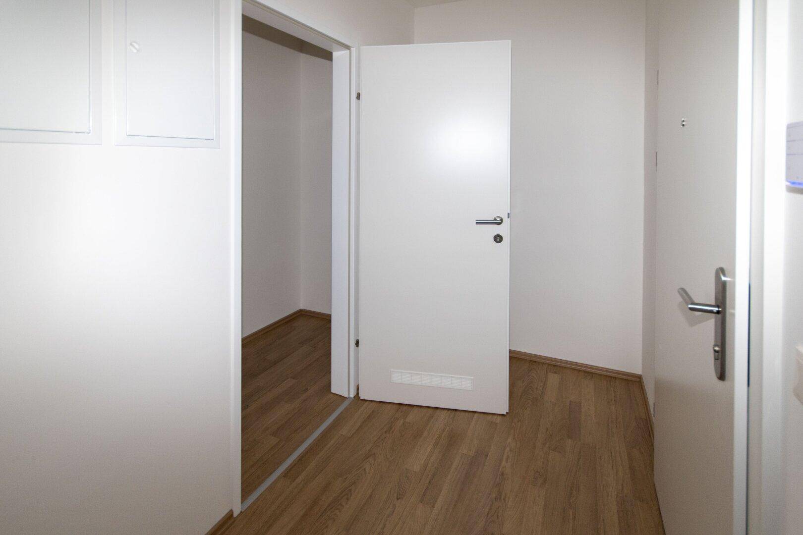 Heller Flur mit Laminatboden und einer offenen Tür, die den Zugang zu einem angrenzenden Raum ermöglicht.
