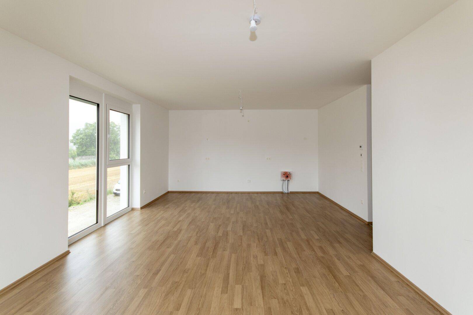 Helles, unmöbliertes Wohnzimmer mit Laminatboden und einem großen Fenster, bereit zur individuellen Gestaltung.