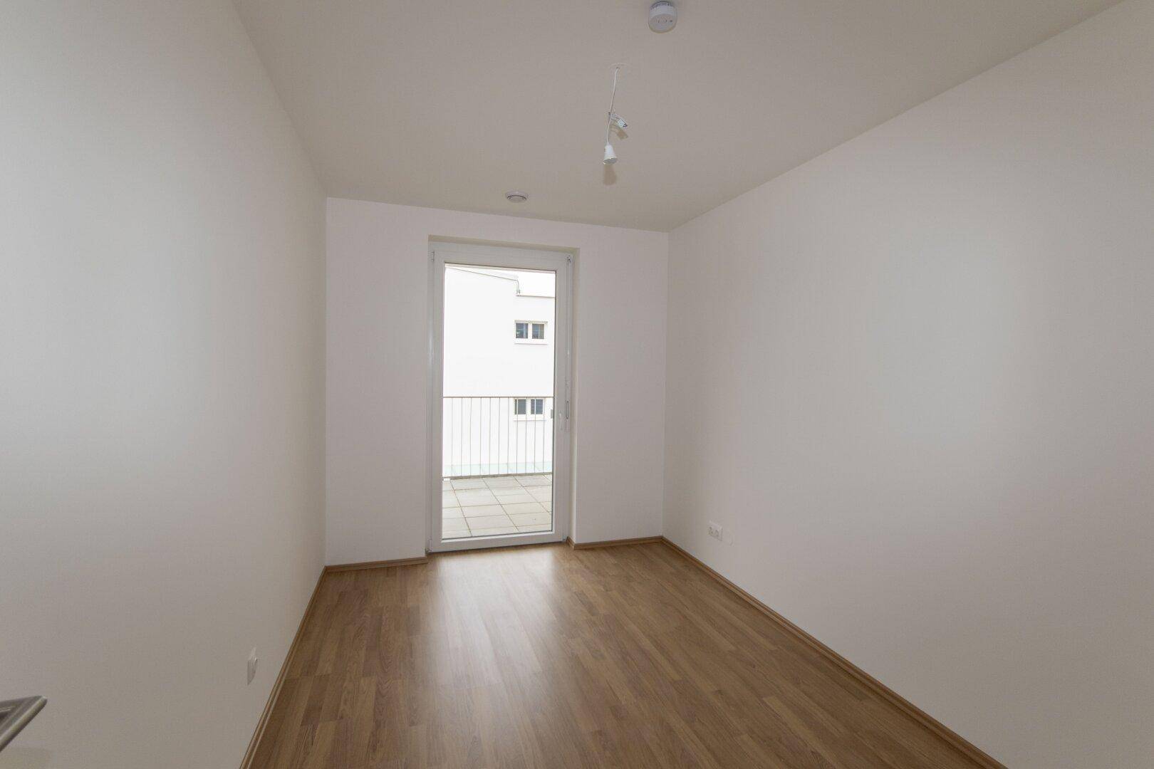 Leeres Schlafzimmer mit Holzboden und Zugang zu einem kleinen Balkon, ideal für Einzelpersonen.