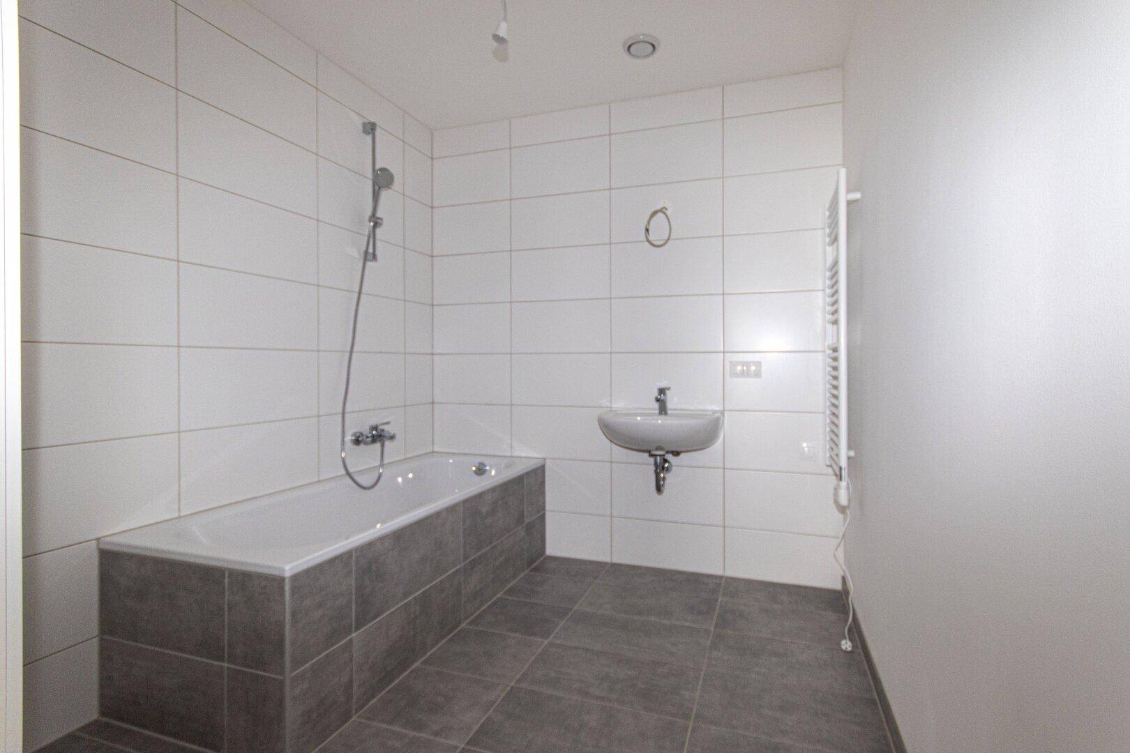 Modernes Badezimmer mit Badewanne, Waschbecken und weißen sowie grauen Fliesen.