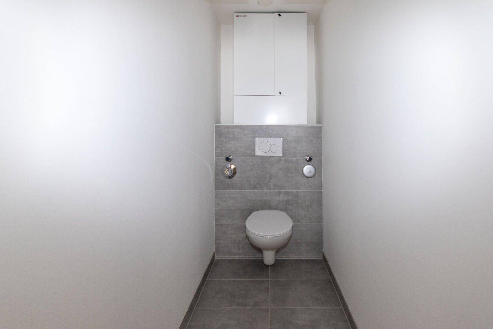 Separates WC mit wandhängender Toilette und grauen Fliesen, minimalistisch gestaltet.