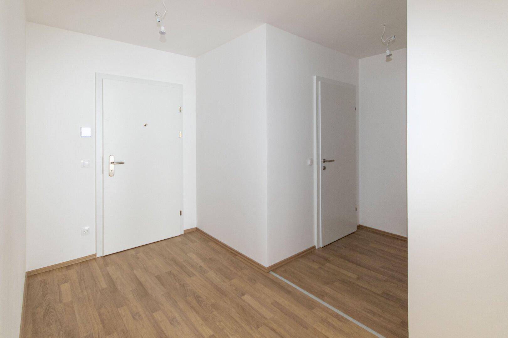 Eingangsbereich mit weißer Tür und hellem Laminatboden, der einen modernen Eindruck vermittelt.