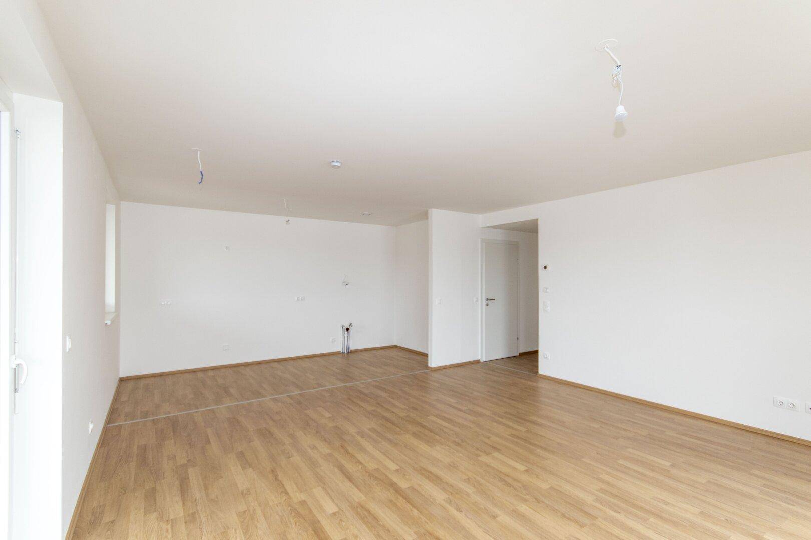 Leerer Küchenbereich mit Anschlüssen für eine Einbauküche und hellem Laminatboden.