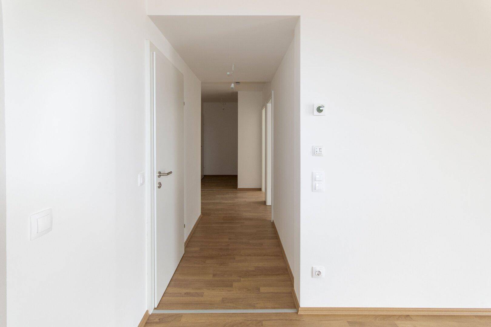 Heller Flur mit Laminatboden und weißen Wänden, der zu weiteren Zimmern führt.
