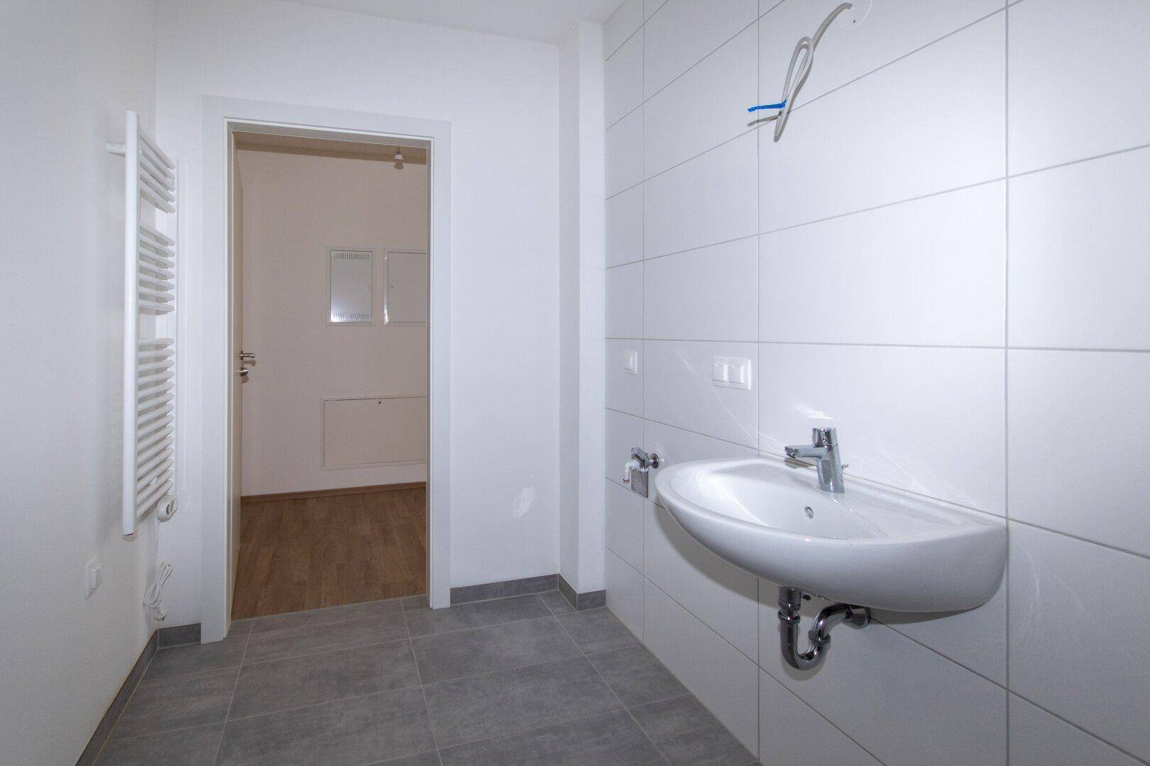 Helles Badezimmer mit modernen Fliesen, Waschbecken und einem beheizten Handtuchhalter.