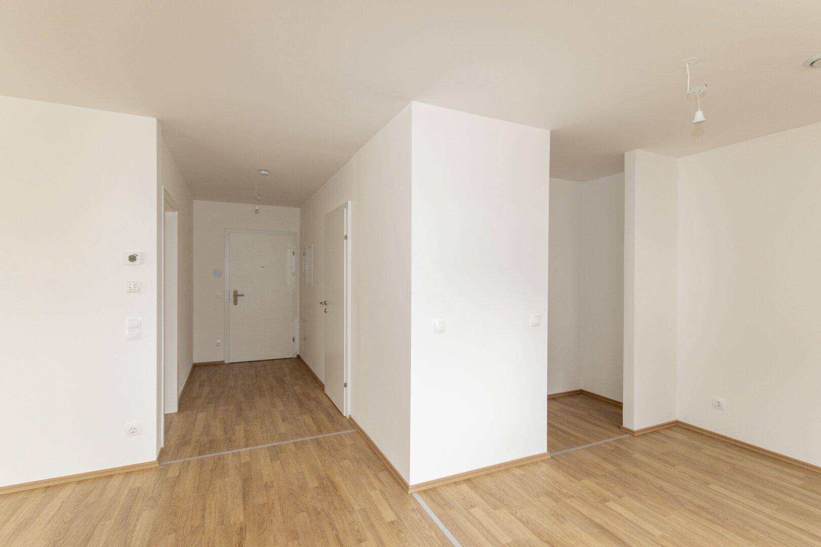 Helle Diele mit modernem Laminatboden und Zugang zu weiteren Räumen in einer Neubauwohnung.
