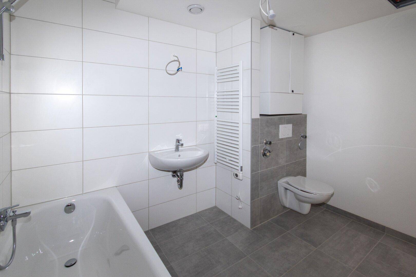 Modernes Badezimmer mit Badewanne, Waschbecken, WC und weiß-grauen Fliesen.