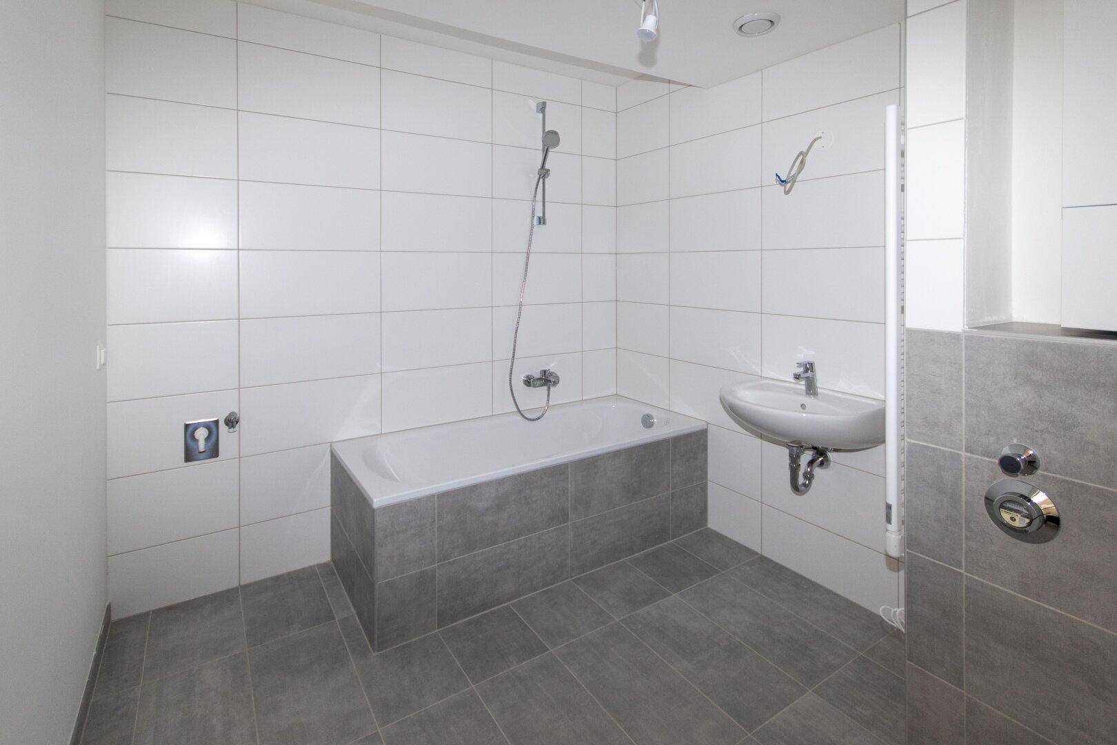 Helles Badezimmer mit Badewanne, integrierter Dusche und modernen grauen Bodenfliesen.