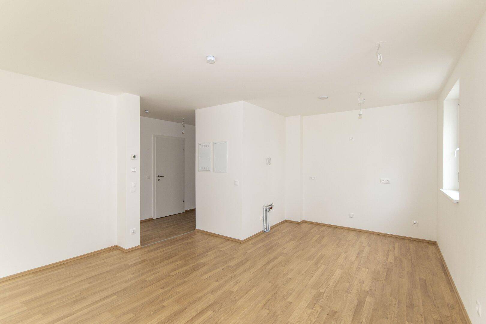 Leerer Küchenbereich mit Laminatboden und Anschlüssen für eine zukünftige Einbauküche.
