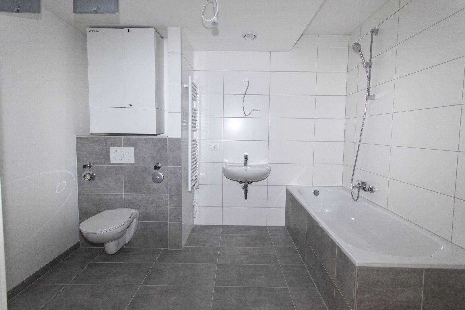 Modernes Badezimmer mit Badewanne, WC und Waschbecken in Grautönen und weißen Fliesen.