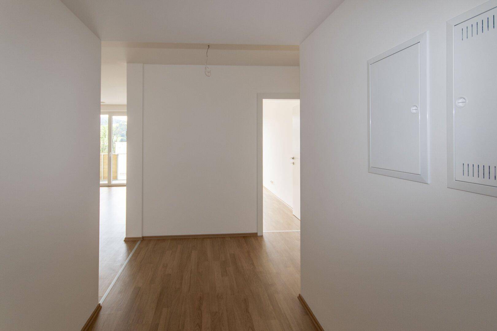 Lichtdurchfluteter Flur mit Laminatboden und Zugang zu Wohnbereich und weiteren Zimmern, mit praktischen Wandpaneelen.