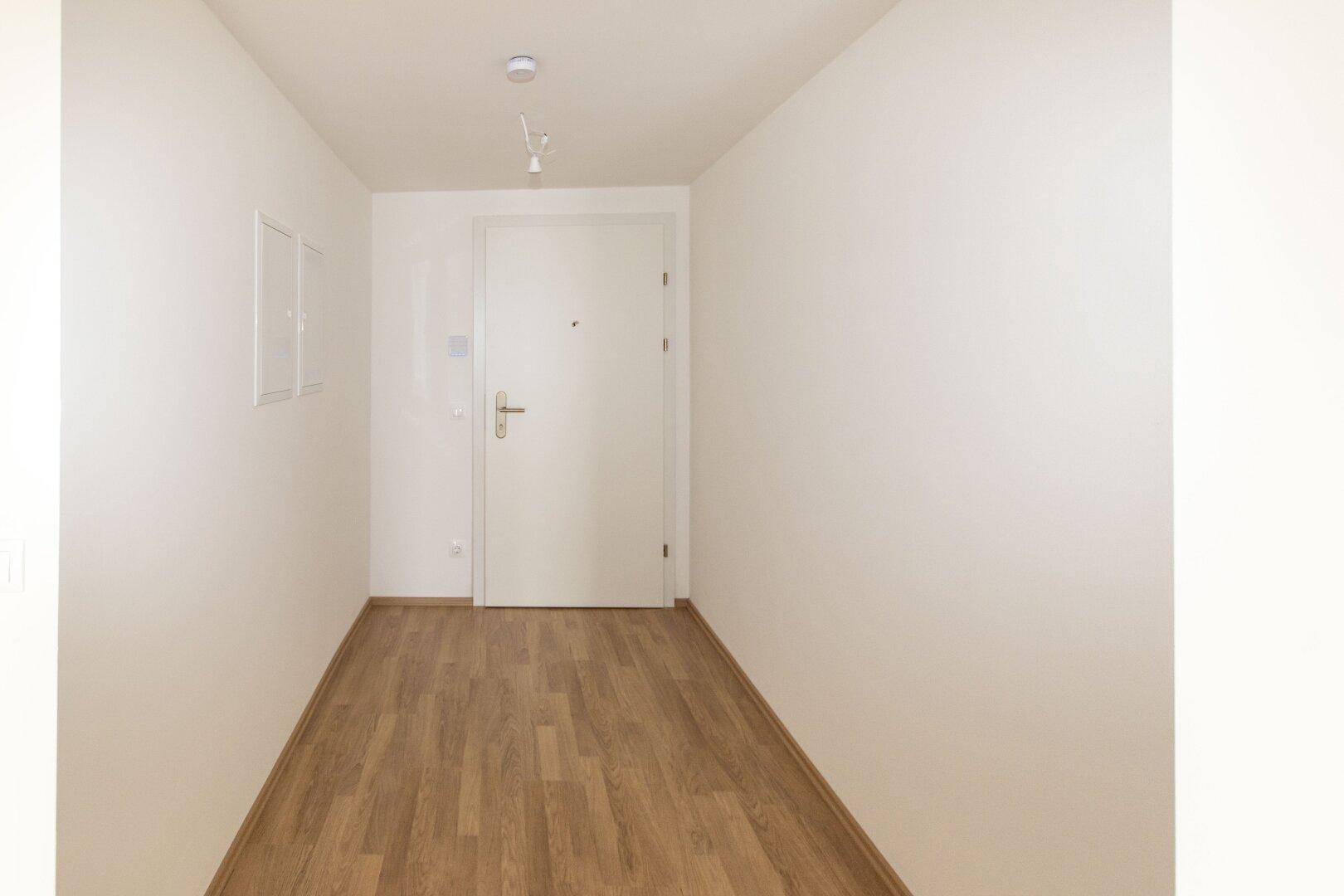 Eingangsbereich mit weißer Tür und hellem Laminatboden, der einen sauberen und einladenden Eindruck vermittelt.