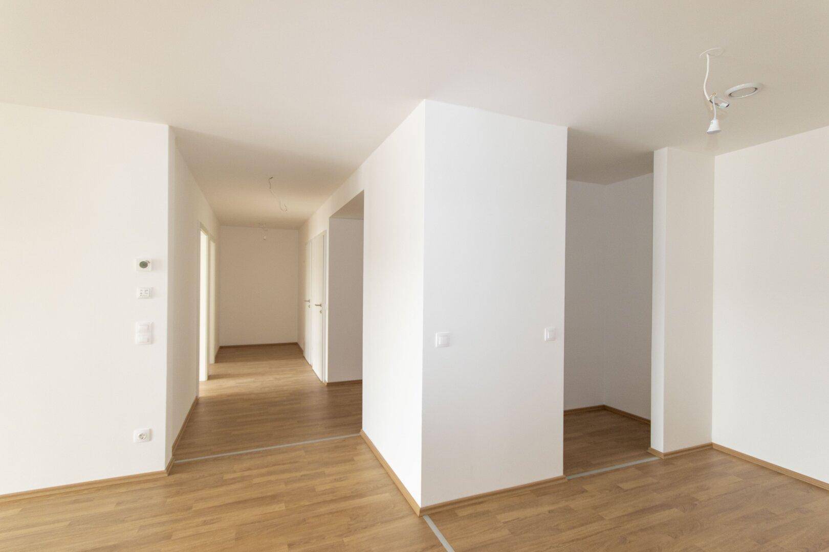 Heller Flur mit Laminatboden und weißen Wänden, der zu verschiedenen Zimmern der Wohnung führt.