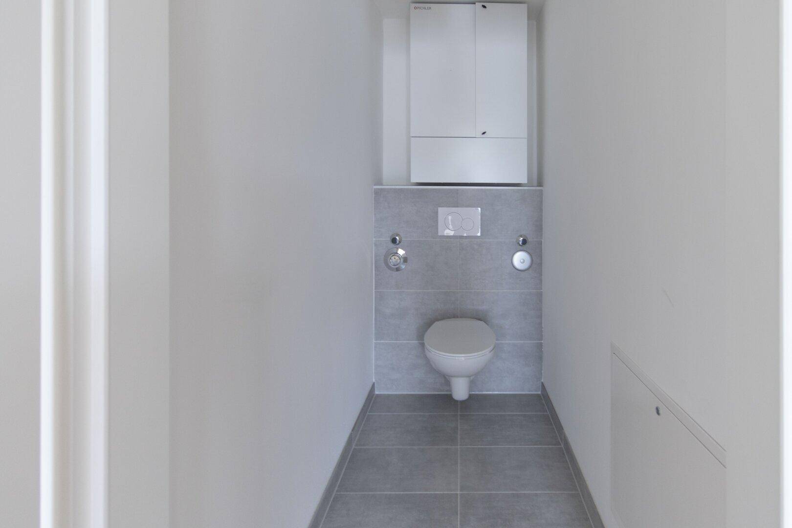 Separates Gäste-WC mit wandhängender Toilette, grauen Fliesen und einem praktischen Wandschrank über der Spülung.