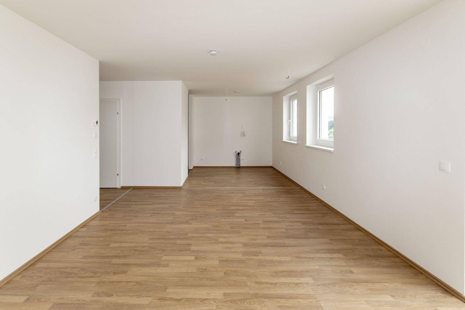 Helles, unmöbliertes Zimmer mit Laminatboden und weißen Wänden, bereit zur individuellen Gestaltung.