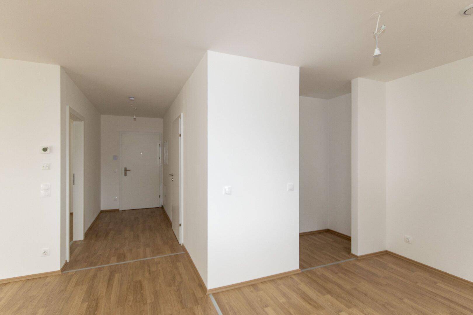 Heller Eingangsbereich mit Laminatboden und weißen Wänden, der zu den verschiedenen Wohnbereichen führt.