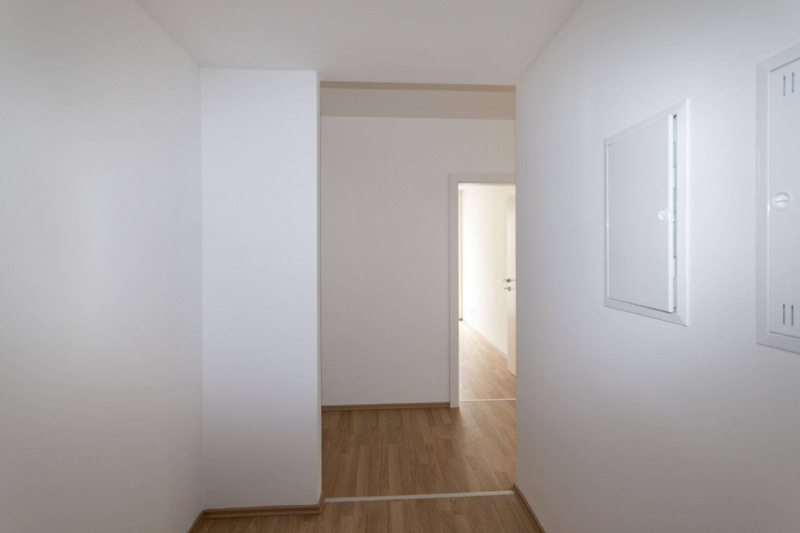 Schmaler, heller Flur mit Laminatboden und weiß gestrichenen Wänden, der zu weiteren Räumen führt.
