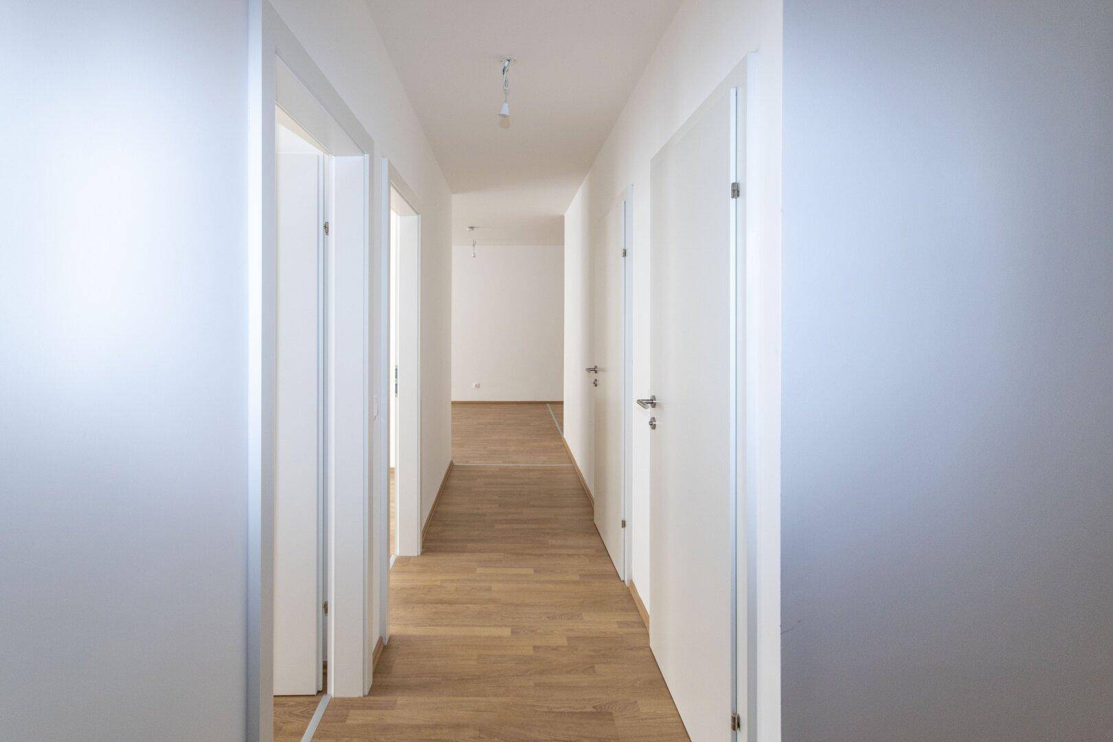 Langer, heller Flur mit Laminatboden und mehreren weißen Türen, die zu den Zimmern führen.